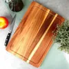 A wooden cutting board with an apple, knife, and olive oil bottle on a light green cloth. Podgląd zdjęcia produktu