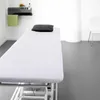 A clean, minimalist room with a treatment table, shelf, and chair. Produktbild-Vorschau