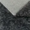 A close-up view of the underside and edge of a dark gray shaggy rug. Produktbild-Vorschau