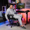 A man is sitting in a gaming chair in a room with colorful lighting, playing a video game. Produktbild-Vorschau
