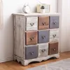 A vintage-style wooden chest of drawers with nine drawers, each with a metal handle. The drawers are in various colors: white, brown, and gray. The chest is placed on a wooden floor against a white wall. Podgląd zdjęcia produktu