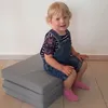 A young child is sitting on a folded gray mattress. Produktbild-Vorschau