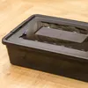 A black plastic storage box with a lid sits on a wooden floor. Anteprima dell’immagine prodotto