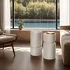 Two white cylindrical side tables are placed in a living room with a large window overlooking a swimming pool and trees. Náhled obrázku produktu
