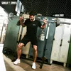 A man is performing a squat exercise with a barbell in a gym setting, with lockers in the background. Produktbild-Vorschau