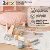 A wooden toy toolbox and accessories are laid out on a textured rug, with a large pink cushion and a play tent in the background. Produktbild-Vorschau