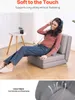 A woman is sitting on a gray floor sofa, wearing headphones and listening to music. The sofa is in a living room setting with a small side table and a plant in the background. A close-up of the fabric is shown at the bottom. Voir les images du produit