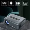 A dark gray projector sits on a textured surface, with a blurred background of a dark green chair and abstract graphics at the top. Voir les images du produit