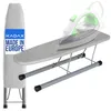 A small ironing board with an iron on it, and a folded ironing board cover next to it. Produktbild-Vorschau