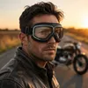 Mann trägt schwarze Vintage-Motorradbrille und abgenutzte Lederjacke, mit Motorrad im Hintergrund unscharf Anteprima dell’immagine prodotto