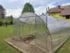 A greenhouse in a garden setting, with a house in the background. Produktbild-Vorschau