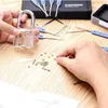A person's hands are shown working with a transparent padlock and lock picking tools on a wooden surface. Produktbild-Vorschau
