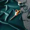 A pair of scissors lies on a piece of teal fabric, with sewing supplies in the background. Náhľad obrázku produktu