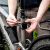 A person is attaching a black device to the seat post of a bicycle. Voir les images du produit