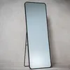 A full-length mirror with a black frame stands on a light-colored wooden floor against a textured gray wall. Náhled obrázku produktu