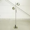 A floor lamp with two circular shades stands on a concrete floor in front of a white wall with horizontal lines. Produktbild-Vorschau