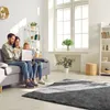 A family is sitting on a sofa in a living room, looking at a laptop. Produktbild-Vorschau