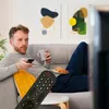 A man is relaxing on a couch, holding a remote control and a mug, with a plate of pastries nearby. Voir les images du produit