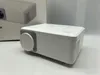 A white mini-projector is shown on a white surface with a white box in the background. Produktbild-Vorschau