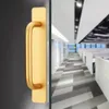 A close-up of a gold door handle on a glass door, with a blurred office interior in the background. Podgląd zdjęcia produktu