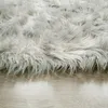A close-up view of a fluffy, high-pile rug with a shaggy texture, resting on a light-colored wooden floor. Produktbild-Vorschau