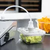 A vacuum sealer is connected to a glass container filled with guacamole, with a bowl of tortilla chips in the background. Produktbild-Vorschau