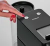 A woman's hand with red nail polish is pressing a button on a black coffee machine. A clear water tank is visible to the left. Náhľad obrázku produktu
