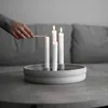A hand is lighting a candle on a round, grey candle holder with four white candles. Produktbild-Vorschau