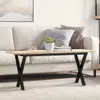 A coffee table with an X-shaped base is placed in front of a sofa in a living room setting. Produktbild-Vorschau
