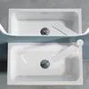 Two identical sinks are shown from a top-down perspective, one above the other. Both sinks are white and feature a modern white faucet and a chrome drain. The background is a textured gray surface. Produktbild-Vorschau
