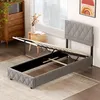 A bed frame with a hydraulic lift mechanism is shown in a bedroom setting. Náhled obrázku produktu