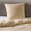 A close-up view of a bed with beige seersucker bedding and a pillow.