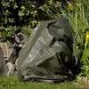 A green tarp covers a large object in a garden setting, with rocks and plants visible. Produktbild-Vorschau