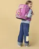 A young girl wearing a backpack and jeans, looking over her shoulder. Voir les images du produit