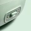 A close-up view of a light green rice cooker with a toggle switch. Produktbild-Vorschau