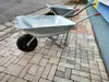 Two wheelbarrows are parked on a paved walkway next to a building. Náhľad obrázku produktu