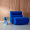 A blue sofa and a striped side table are placed against a wooden wall. Produktbild-Vorschau