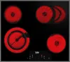 A top-down view of a black ceramic glass induction cooktop with four heating elements glowing red. The brand name 'Beko' is visible on the control panel. Produktbild-Vorschau