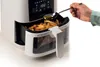 A hand is adding oil to french fries in an air fryer. Náhľad obrázku produktu