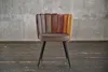 A chair with a multi-colored backrest and a brown seat, standing on a wooden floor in front of a concrete wall. Produktbild-Vorschau