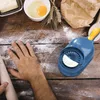 A person's hands are shown preparing dough on a wooden table, with ingredients like butter, eggs, and flour scattered around. A blue and yellow dumpling maker is prominently featured. Podgląd zdjęcia produktu