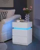 A white LED-lit nightstand next to a sofa, with a vase of flowers and a cup of tea on top. Náhľad obrázku produktu