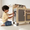 A young boy is playing with a wooden toy kitchen. Podgląd zdjęcia produktu