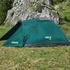A green camping tent is set up on a grassy slope with a rocky mountain in the background. Náhled obrázku produktu