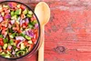 A bowl of chopped salad with a wooden spoon on a rustic red wooden table. Produktbild-Vorschau