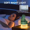 A woman sleeping in a bed next to a green humidifier fan with a night light. Produktbild-Vorschau