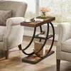 A rustic industrial-style side table with three shelves is placed between two upholstered armchairs next to a window. Produktbild-Vorschau