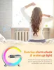 A woman waking up in bed with a sunrise alarm clock next to her. Produktbild-Vorschau