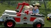 Lego characters in a Jurassic Park jeep driving through a grassy, wooded area. Produktbild-Vorschau