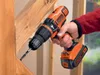 A person is using a Black & Decker cordless drill to drill into a wooden beam. Produktbild-Vorschau
